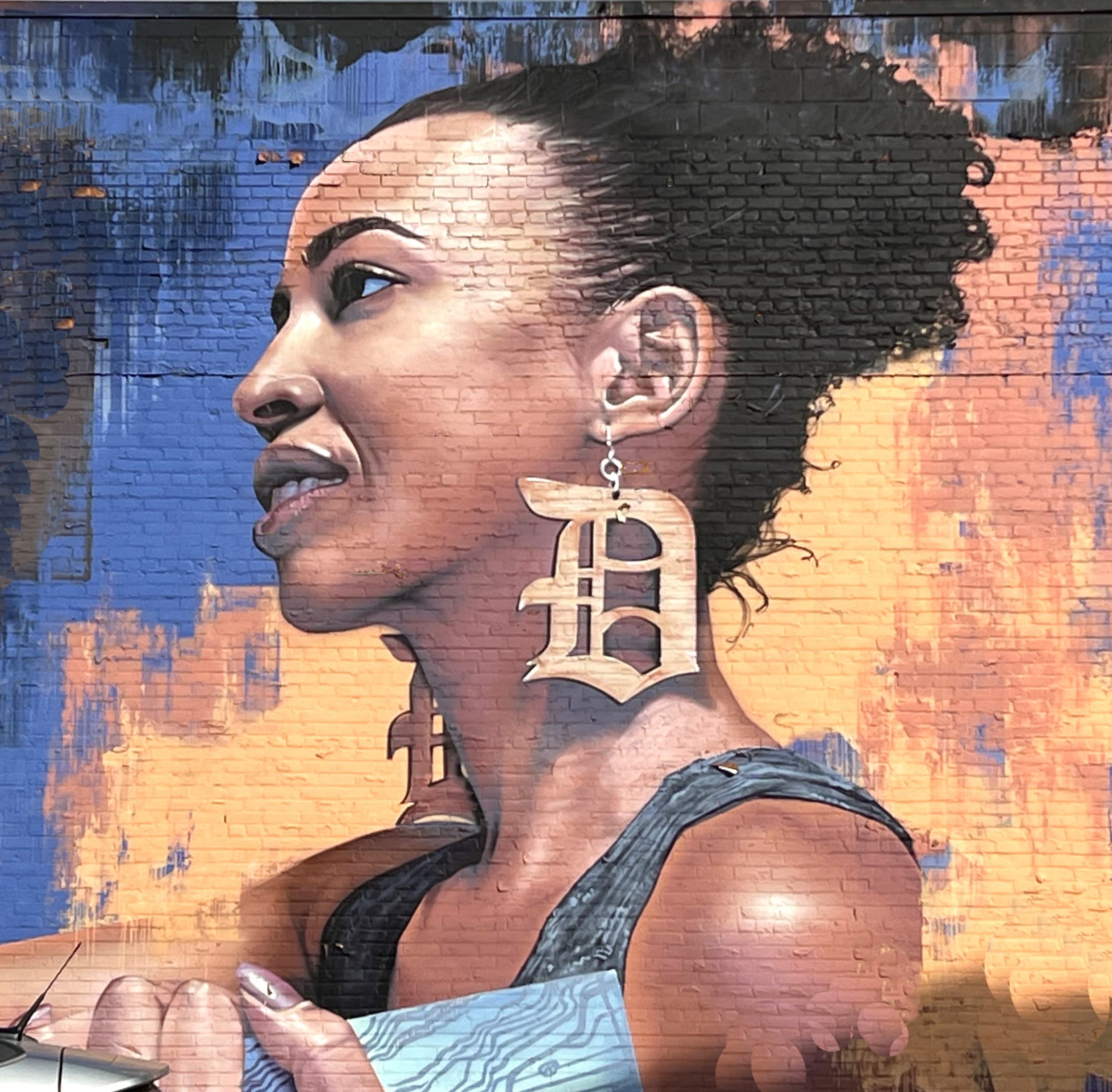 Detroit Eastern Market mural by artist Richard Wilson includes an image of a young woman wearing large gold earrings in the iconic Old English D-style.