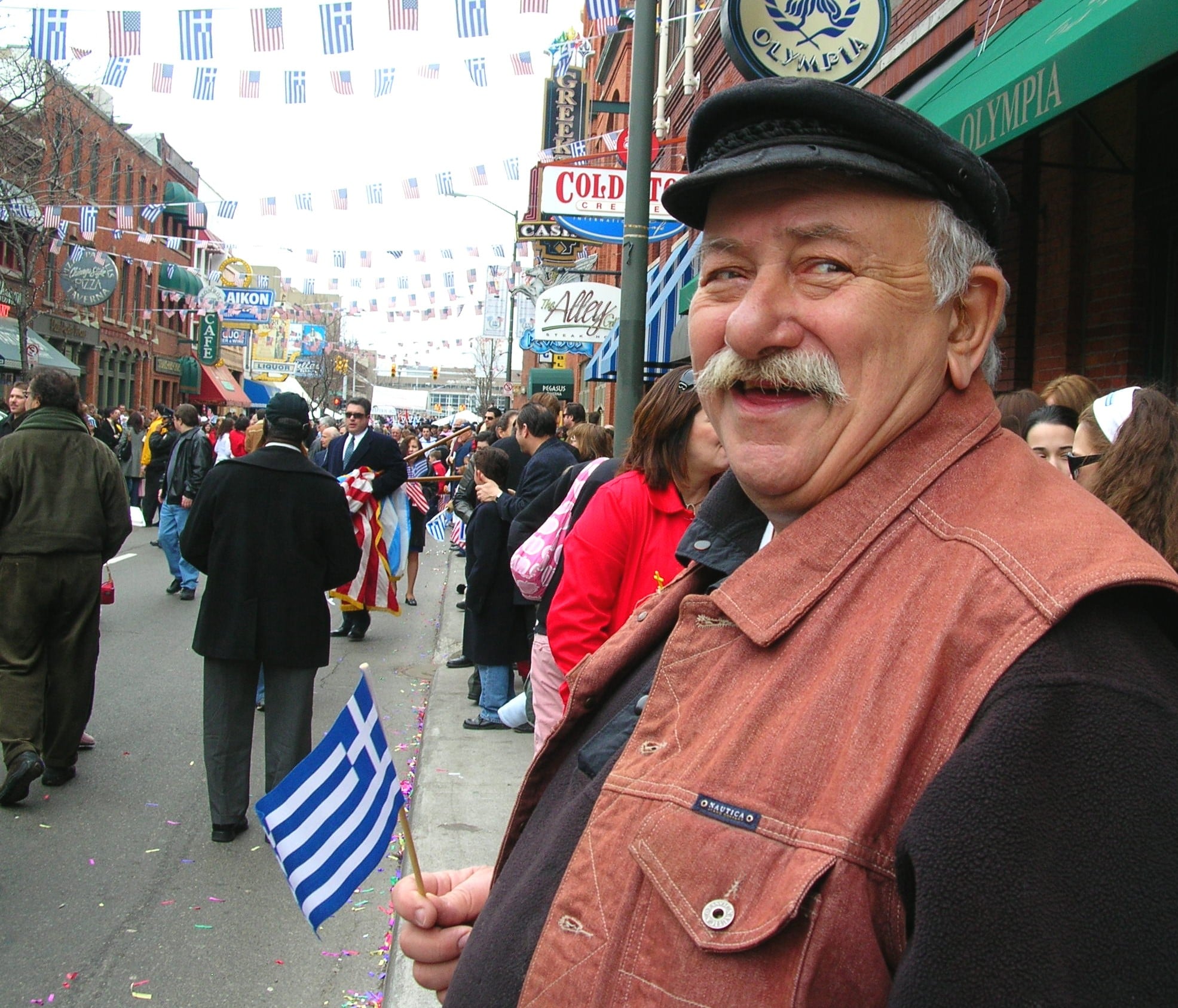 Man watching the Greek Independence Day Parade in Detroit’s Greektown -- displays a Greek flag.